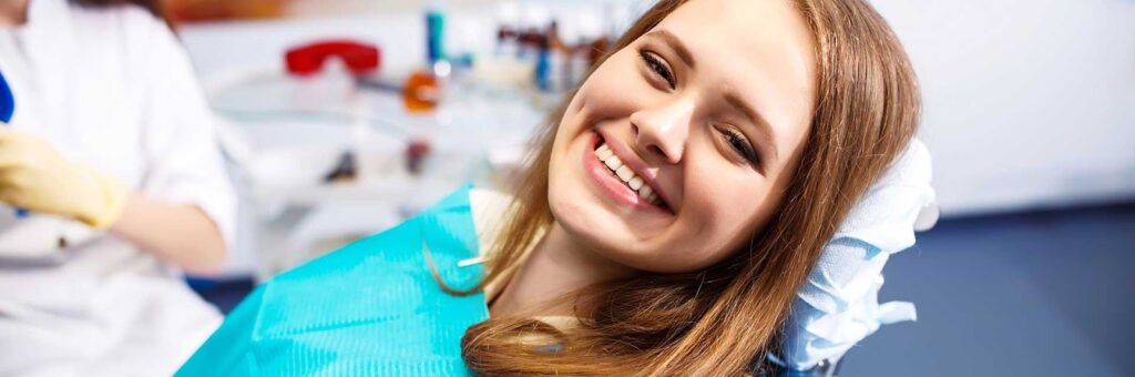 A smiling female patient reclines in a dental chair with a blue bib at family dentistry.