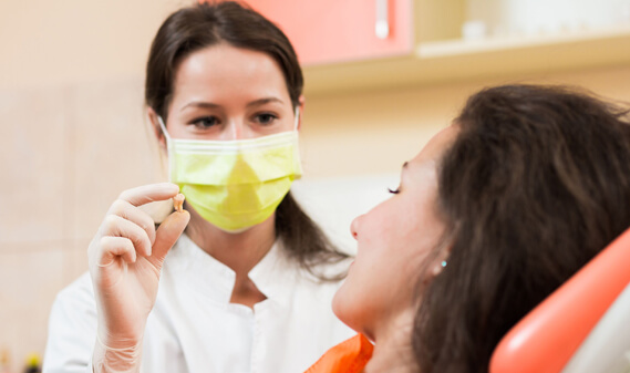 An oral surgeon showing a wisdom teeth to her patient after the wisdom tooth extraction oral surgery.