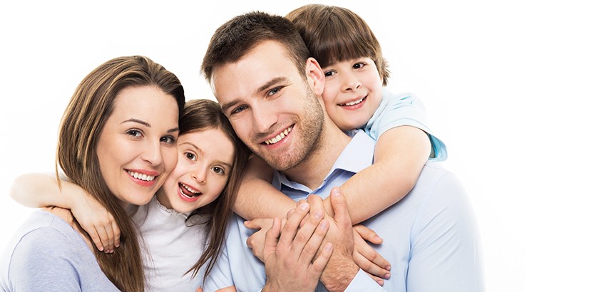 A smiling family of four, parents embracing their two happy children at a family dentist near them.
