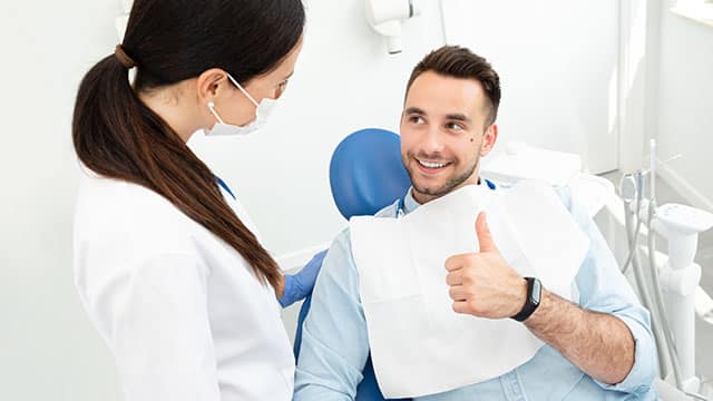 A handsome young man at an oral and maxillofacial surgeon's office showing a thumbs-up after his dental oral surgery.