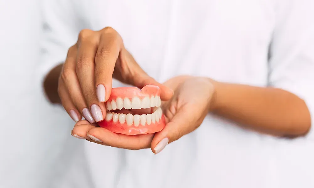Family dentist holding a set of complete dentures in clean, well-manicured hands against a white coat background.