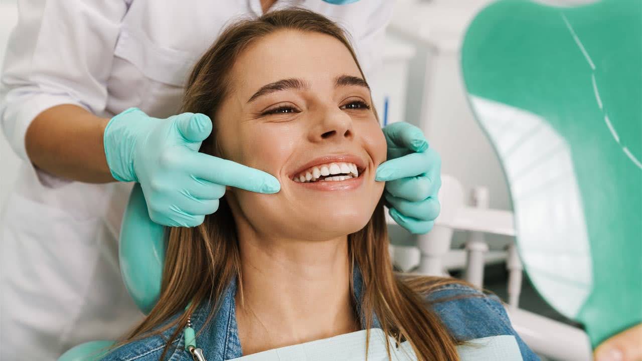A smiling woman at the dental hygienist's office getting examined by her hygienist.