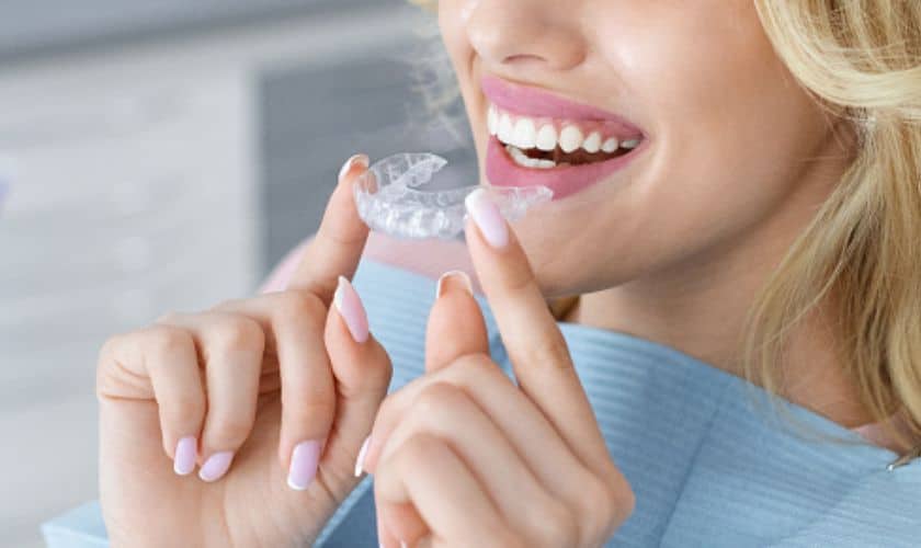 A smiling woman holding clear aligners, a modern alternative to metal braces and traditional braces for teeth.