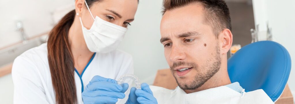A dentist explaining how clear aligners braces work to a male patient as an alternative to metal braces and traditional braces for teeth.