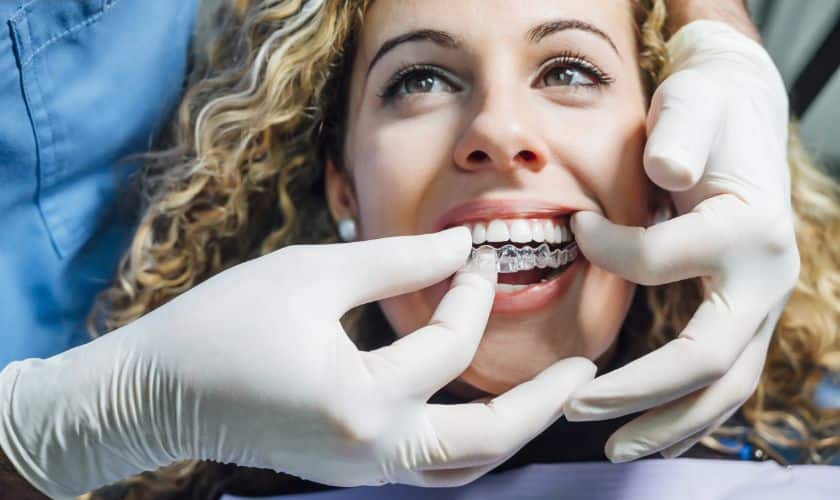 Dentist fitting Invisalign aligners on a smiling patient, showcasing Invisalign vs braces and treatment duration.